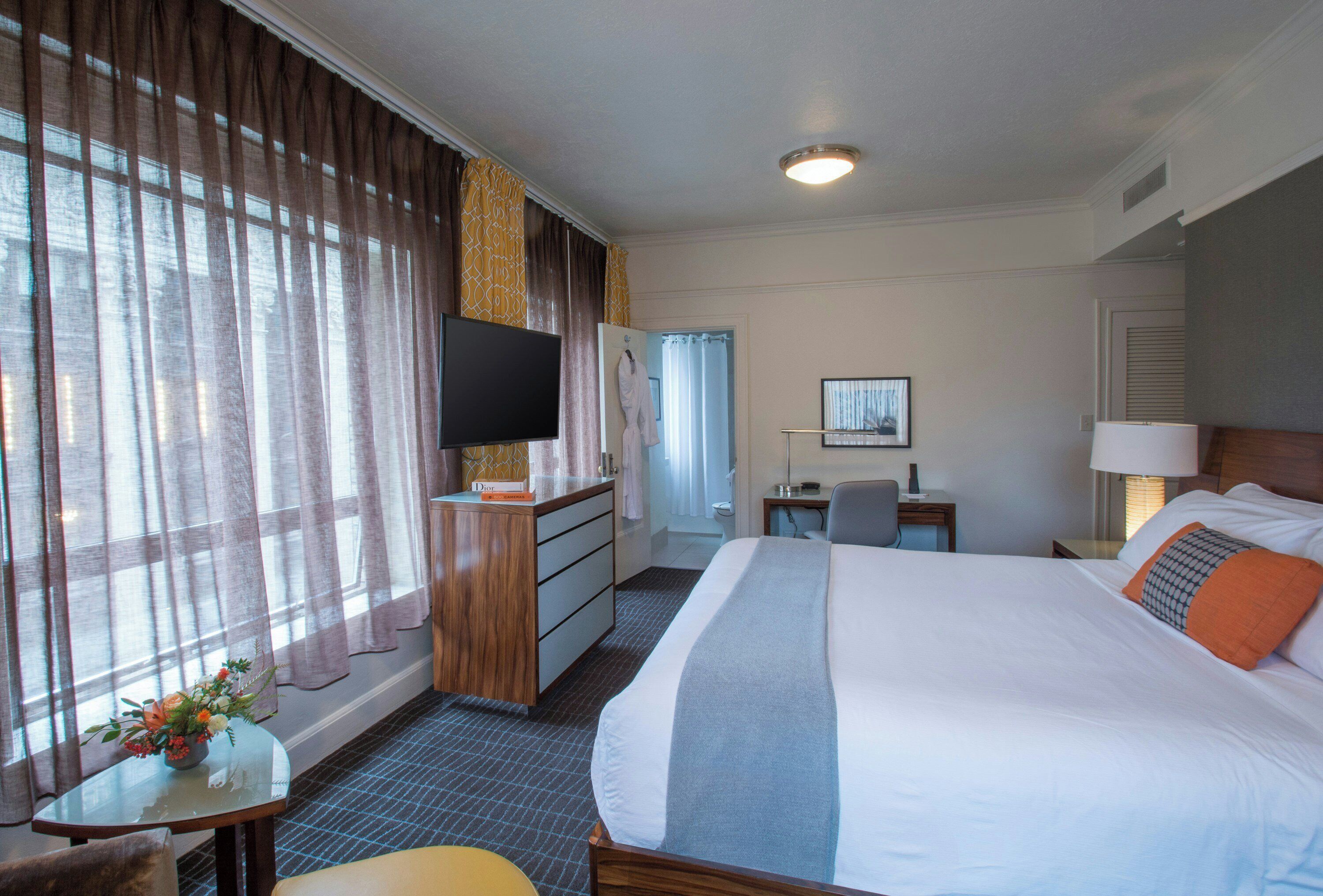 Habitación de hotel con cama, escritorio, televisión y ventana con cortinas.