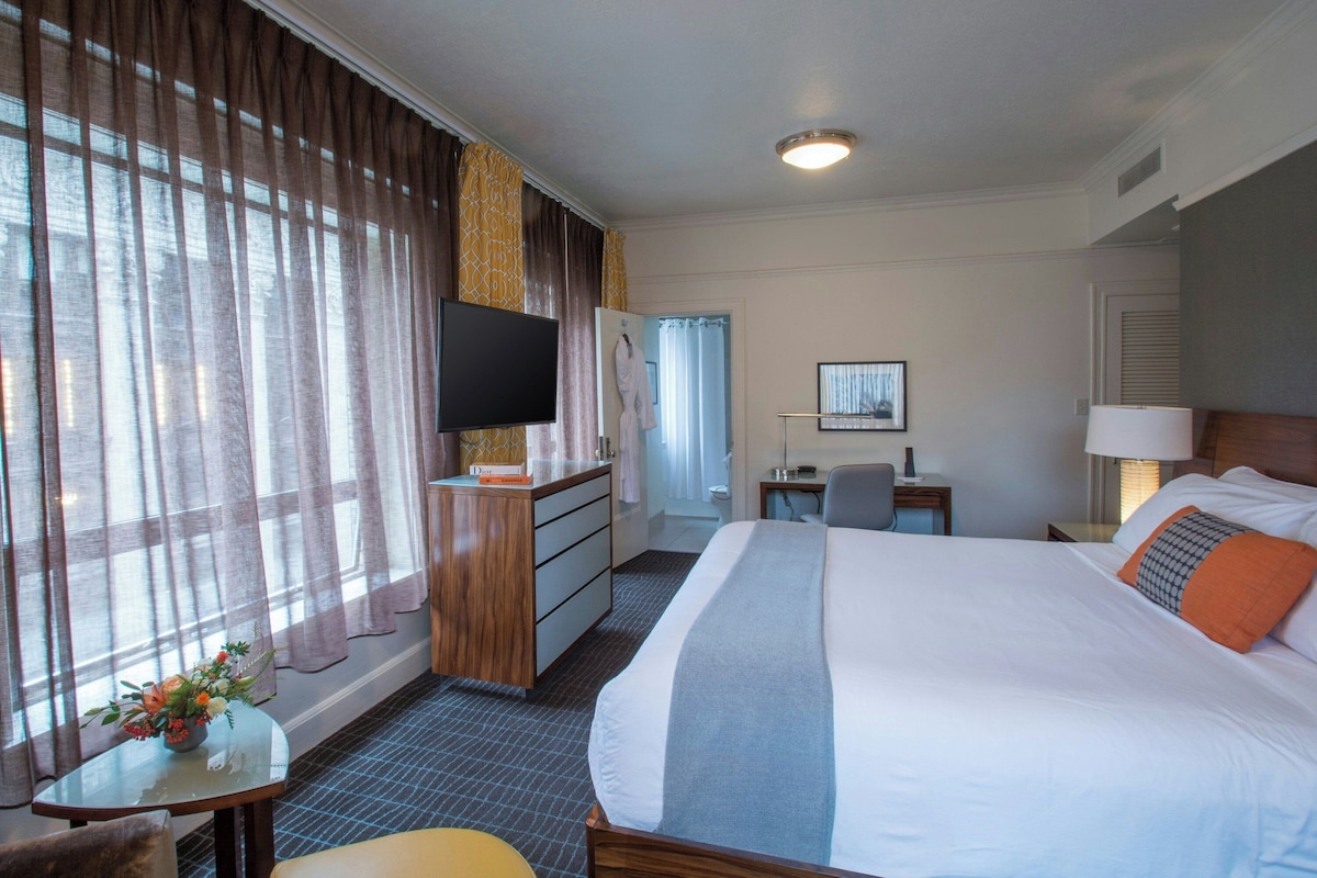 A hotel room with a bed, a desk, a television, and a window with curtains.