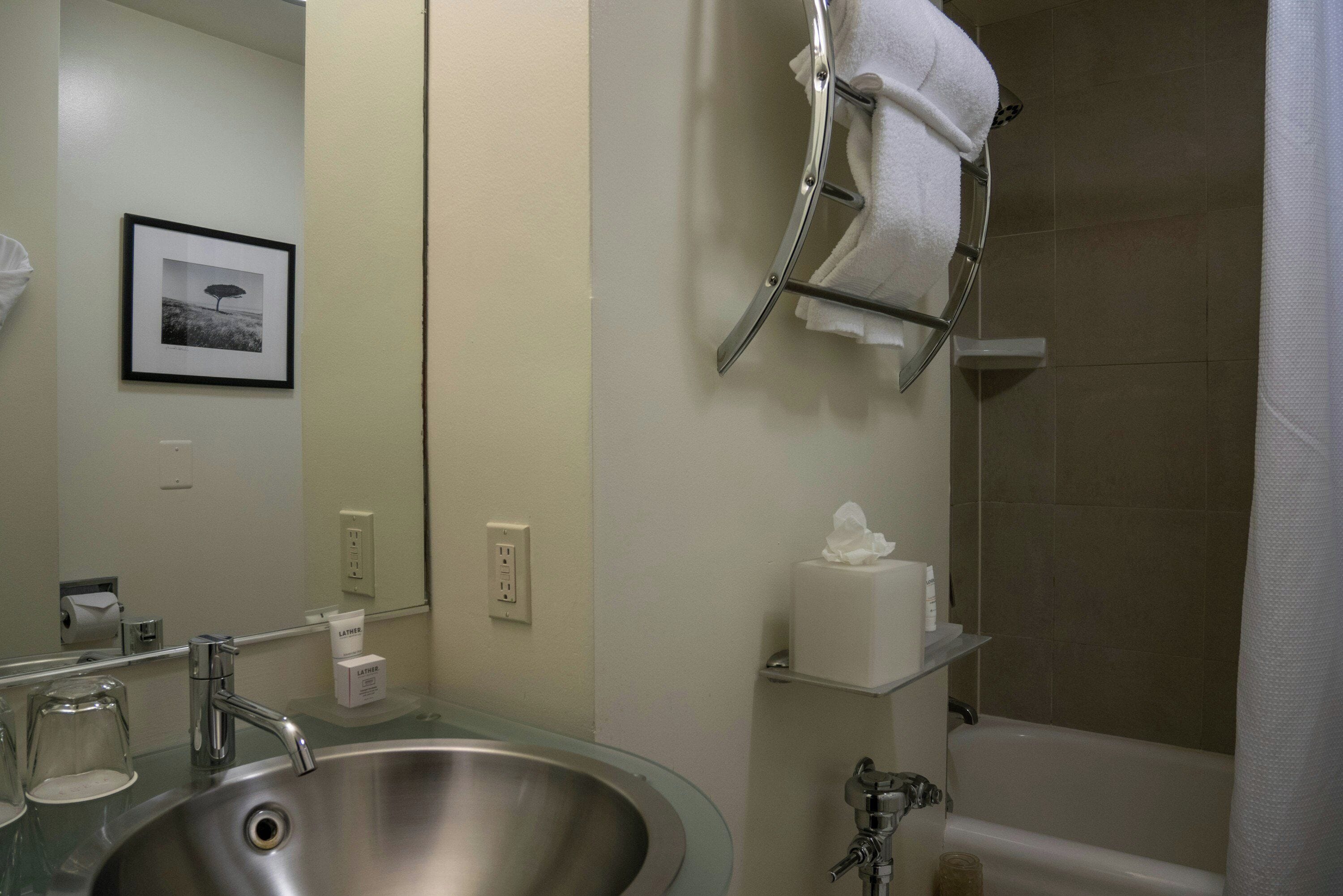 A bathroom with a sink, mirror, towel rack, toilet paper dispenser, and a bathtub.