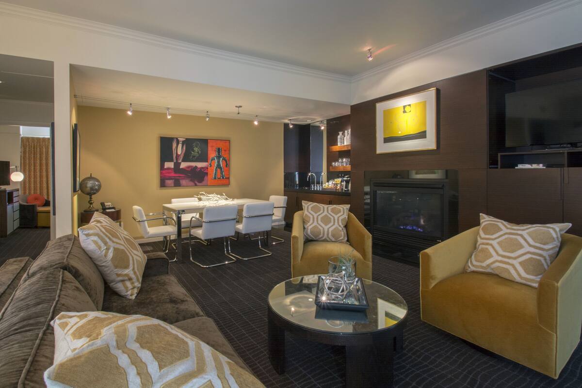 A modern living room with a sofa, armchairs, a coffee table, a fireplace, and a television.