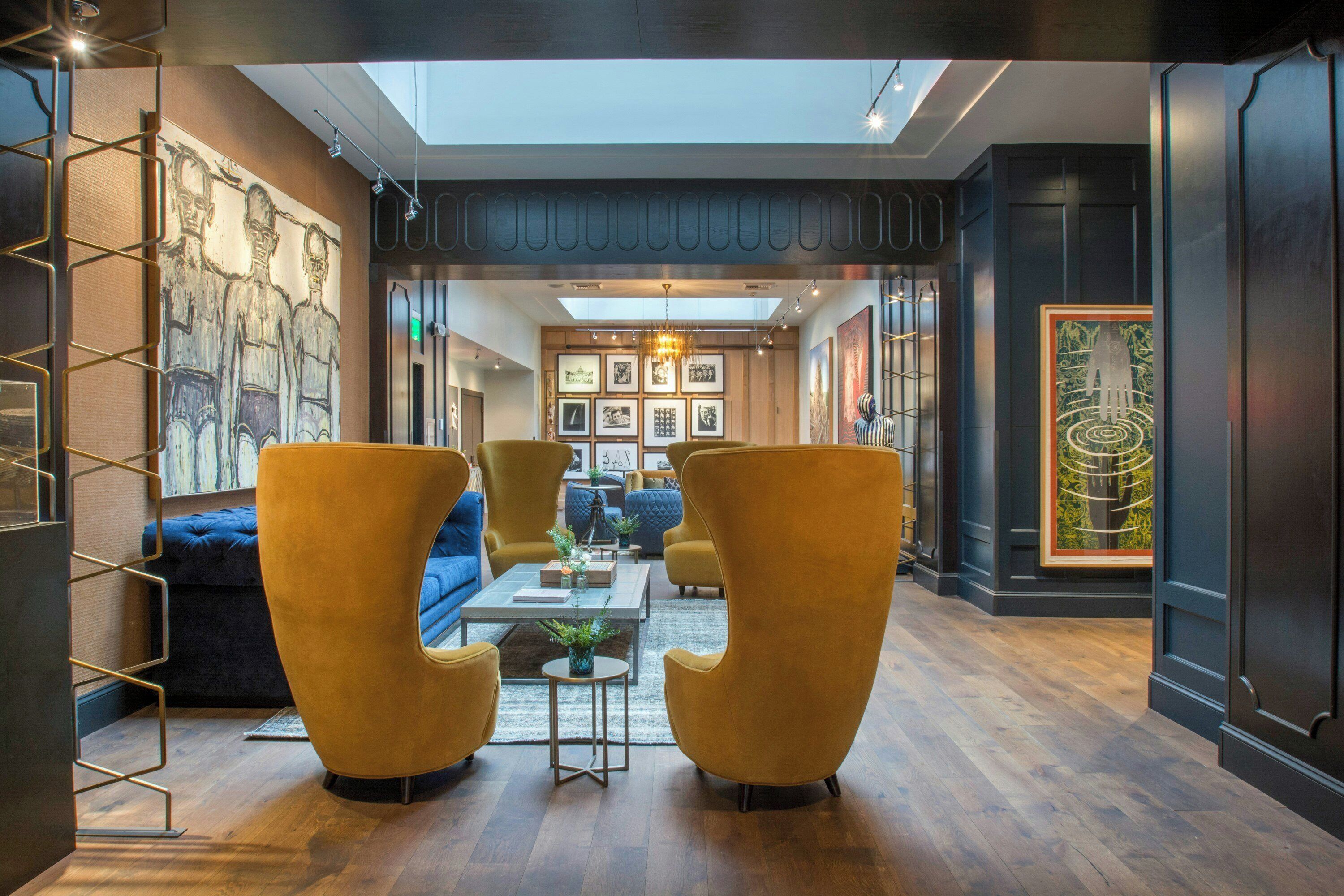 Un intérieur moderne avec un plafond haut, une verrière et un espace salon central agrémenté de fauteuils et d’un canapé.