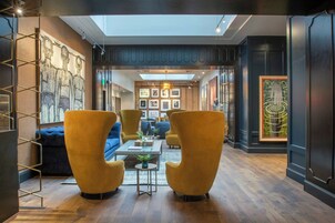 Un intérieur moderne avec un plafond haut, une verrière et un espace salon central agrémenté de fauteuils et d’un canapé.