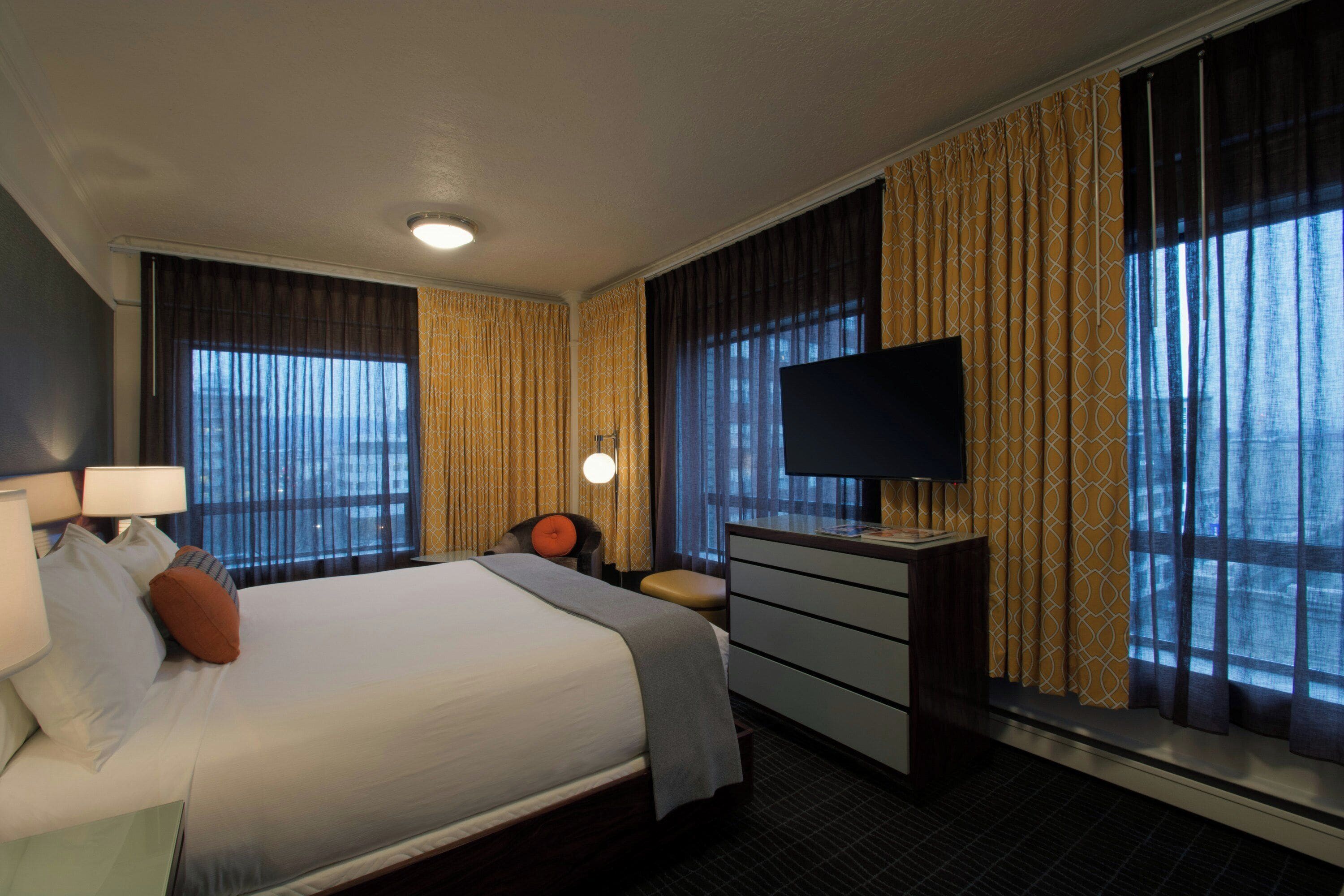 A hotel room with a bed, a desk, a television, and curtains.