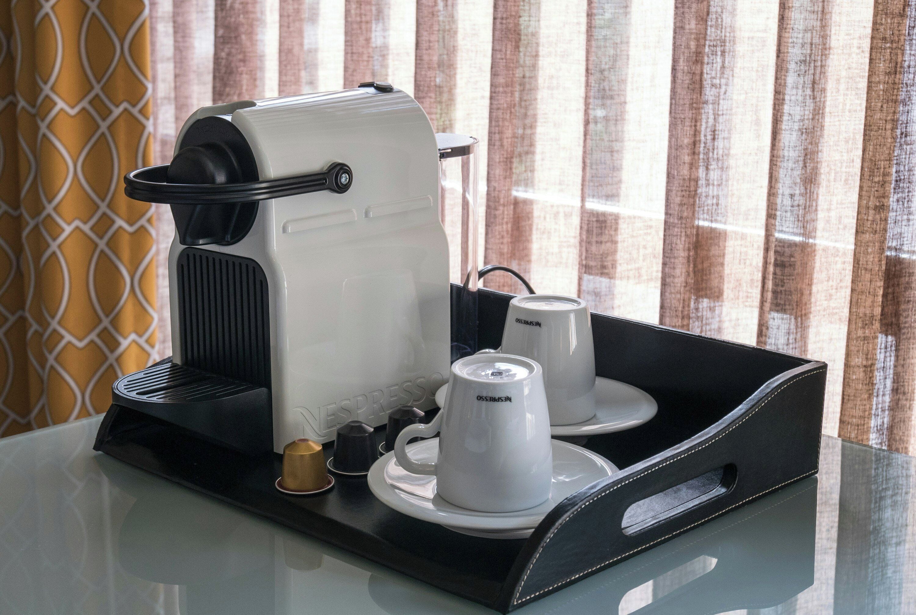 Een koffieapparaat met twee bekers en een kopje koffie op een dienblad.