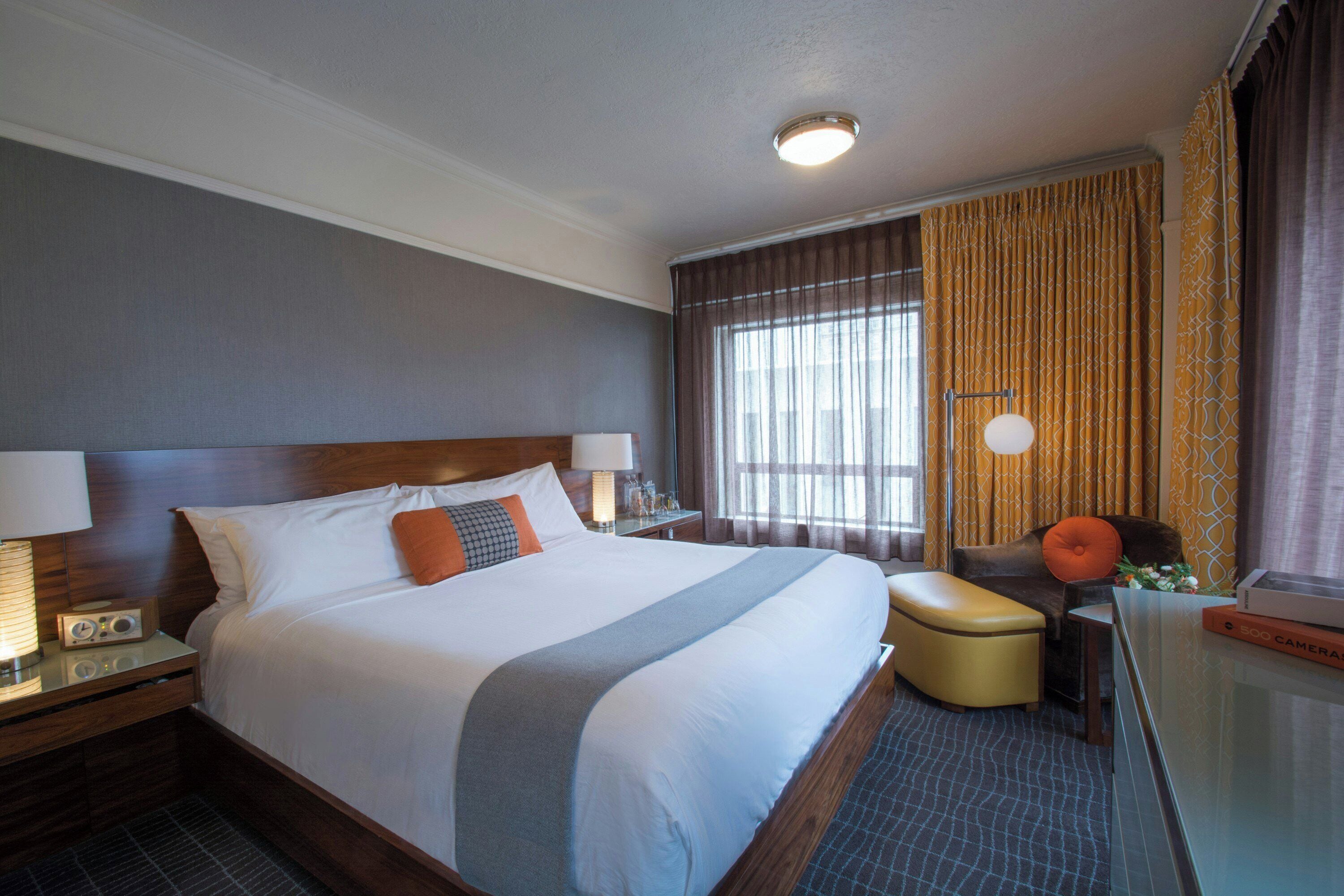 A hotel room with a large bed, bedside lamps, a desk with a lamp, a chair, a window with curtains, and a ceiling light.
