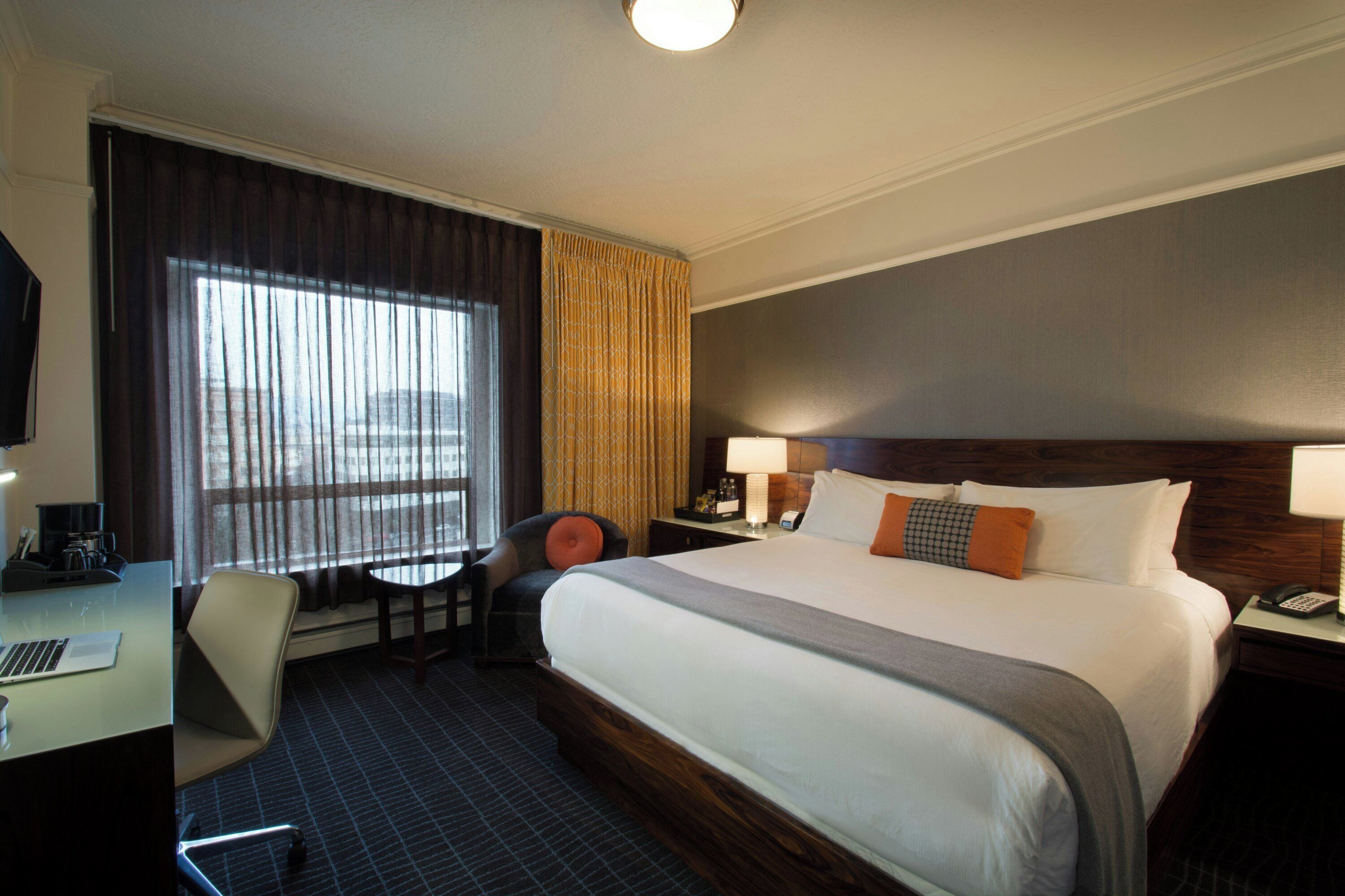 A hotel room with a large bed, a desk with a chair, a television, and a window with curtains.