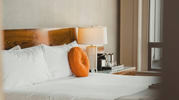 Una habitación de hotel con cama, almohadas, lámpara, mesita de noche y ventana.
