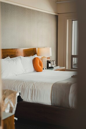 A hotel room with a bed, pillows, a lamp, a nightstand, and a window.