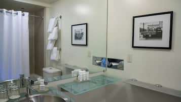 A modern bathroom with a glass sink, a shower, and two framed photographs on the wall.