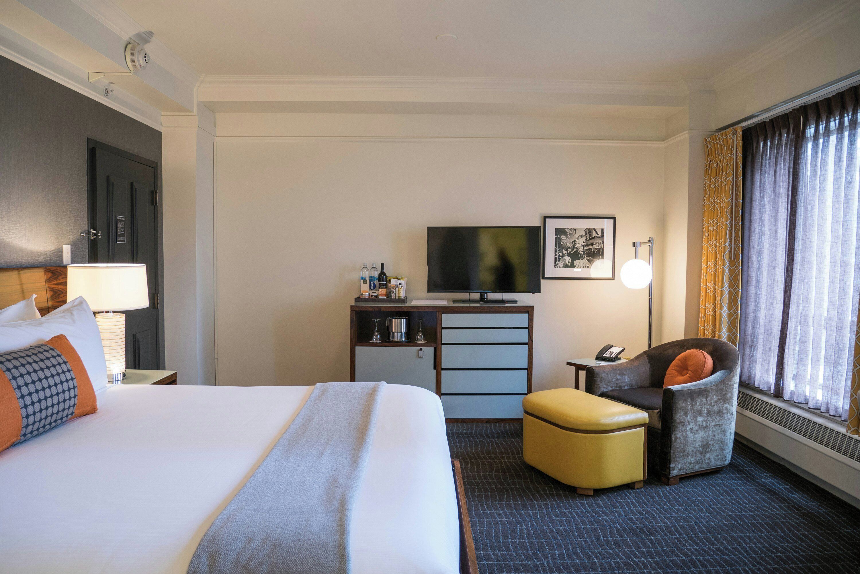 A hotel room with a bed, a desk with a television, a chair, and a window with curtains.