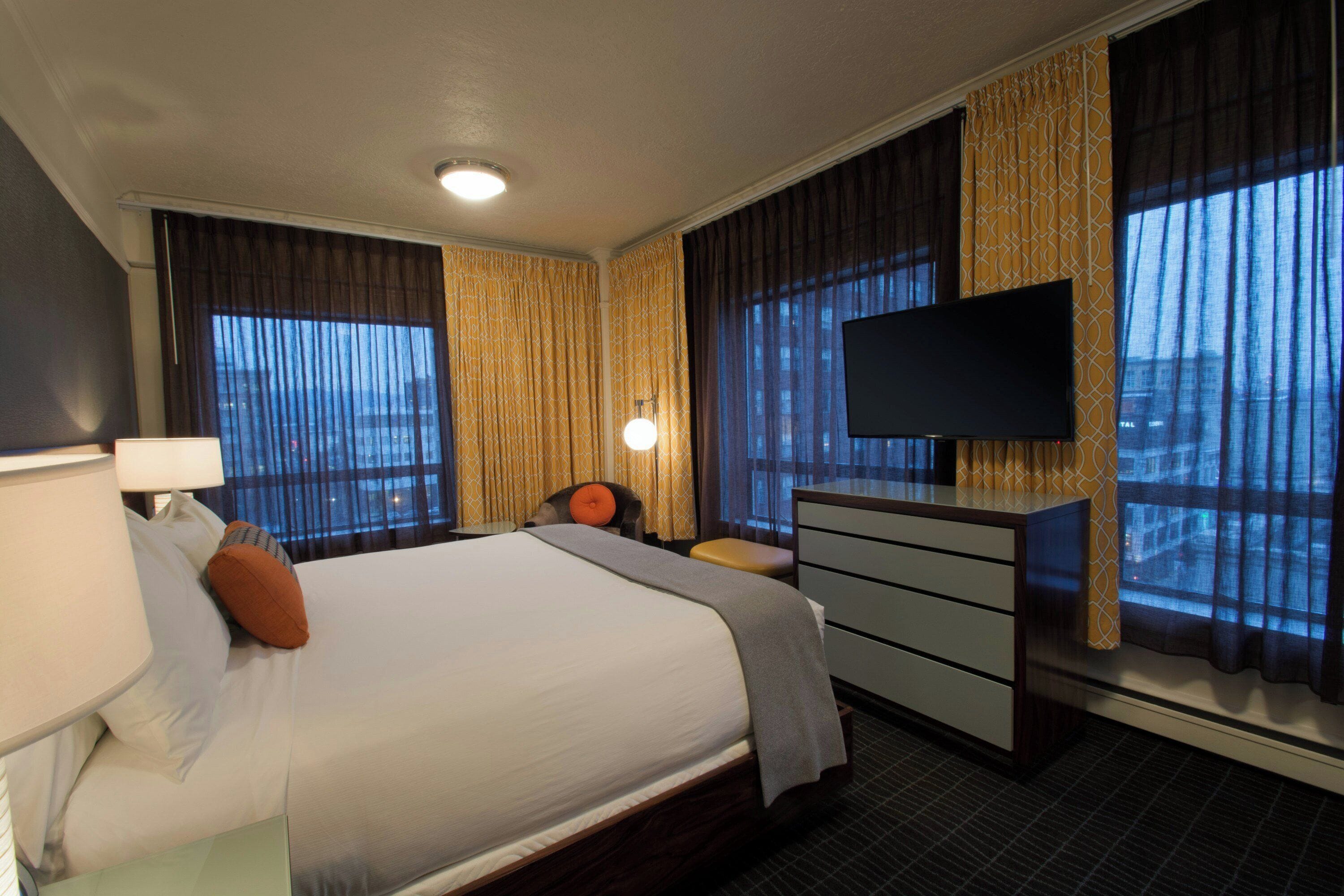 A hotel room with a large bed, a flat-screen TV mounted on the wall, a desk, and a chair.