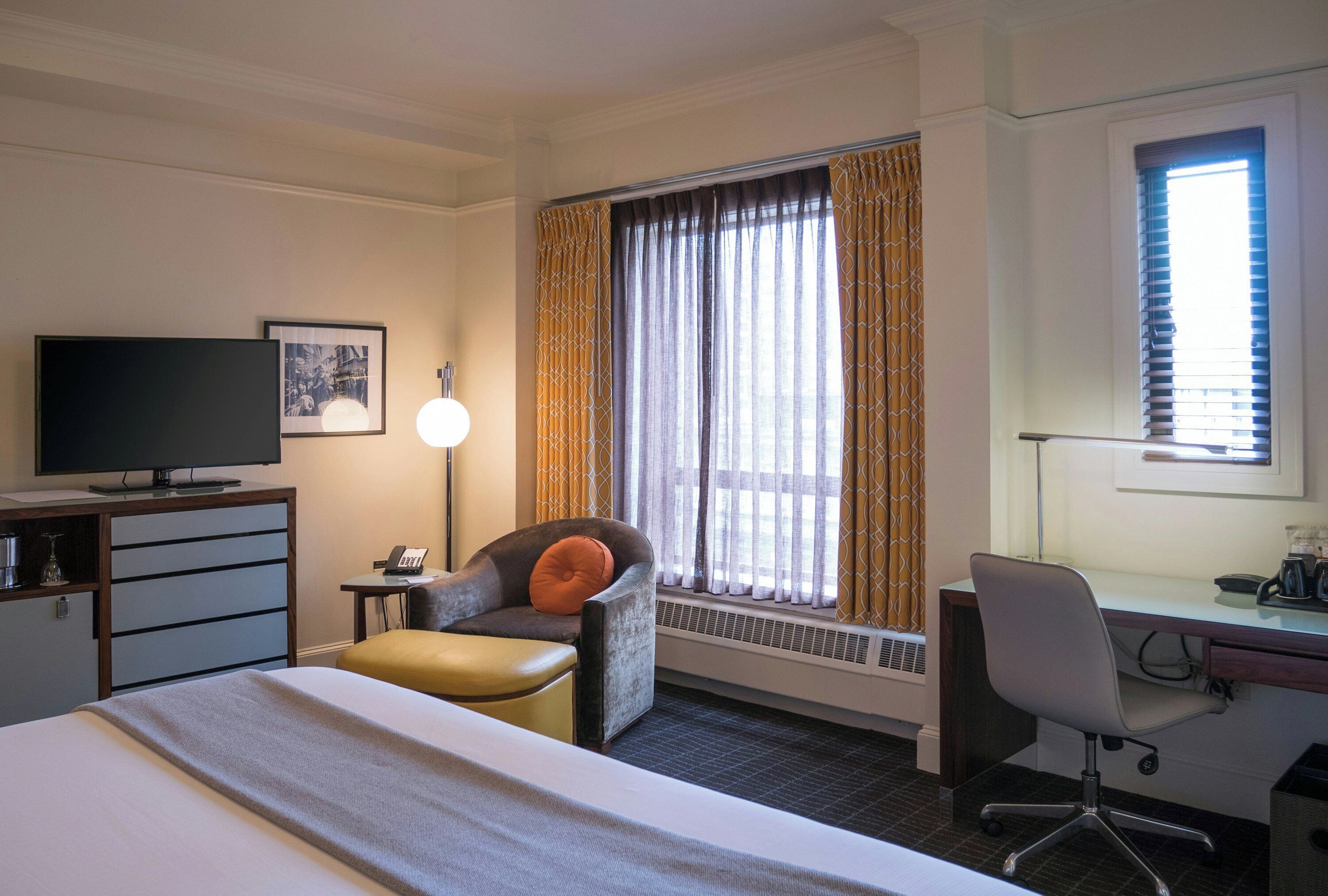 A hotel room with a bed, a desk, a chair, a television, and a window with curtains.