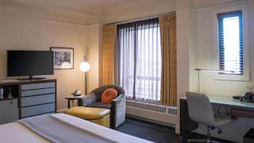 A hotel room with a bed, a desk, a chair, a television, and a window with curtains.
