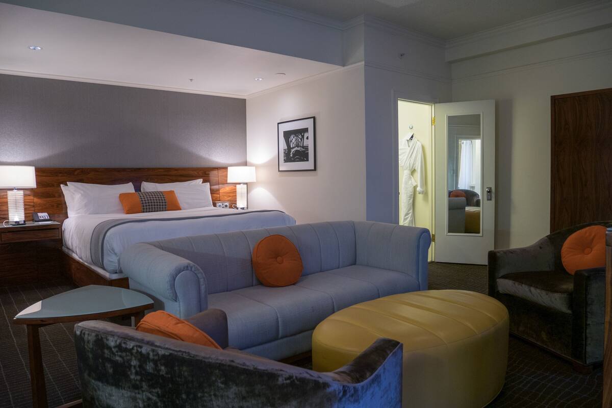 A hotel room with a bed, a sofa, a chair, and a small table.