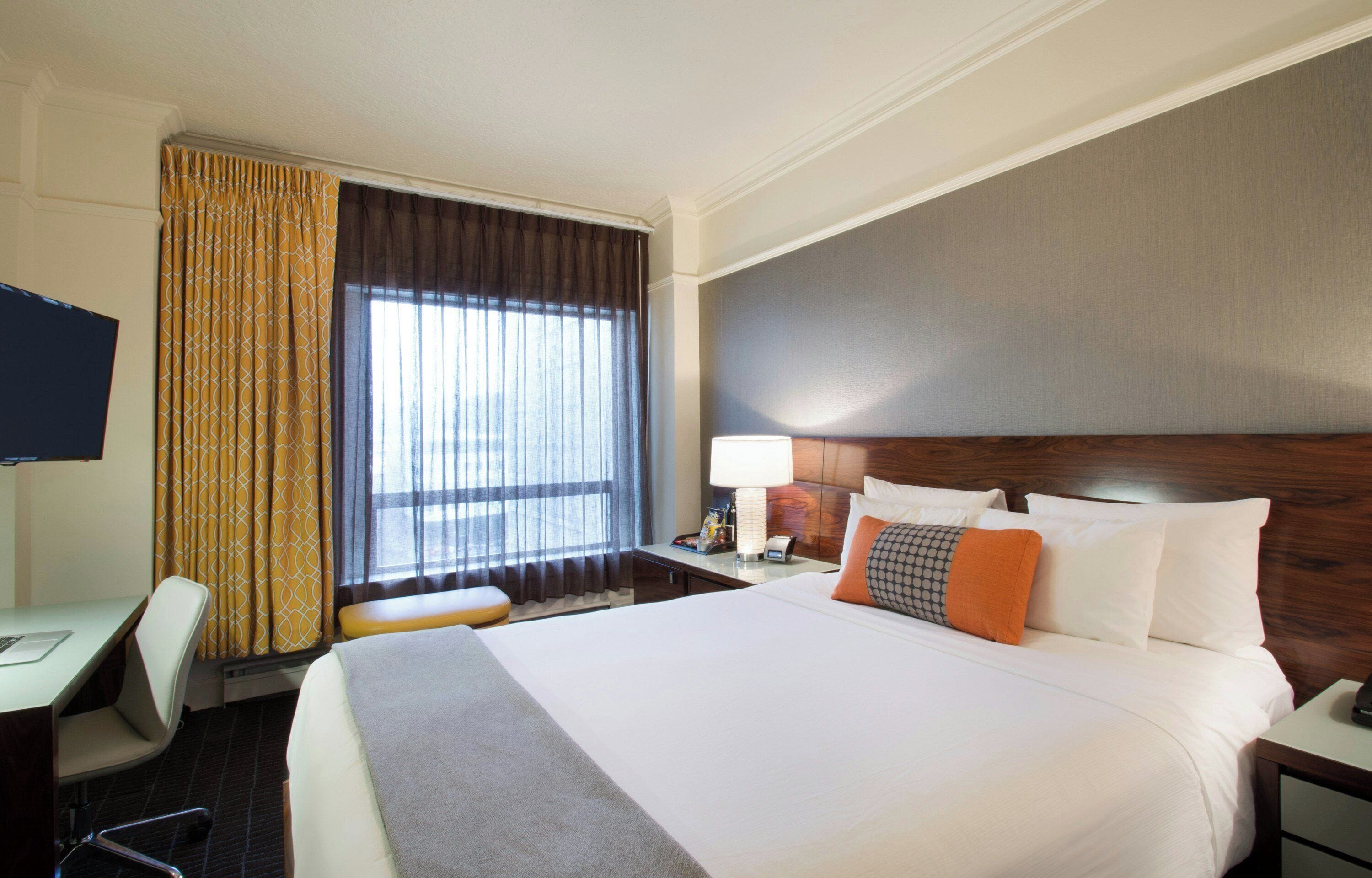 A hotel room with a large bed, a desk, a chair, a TV, and a window with curtains.