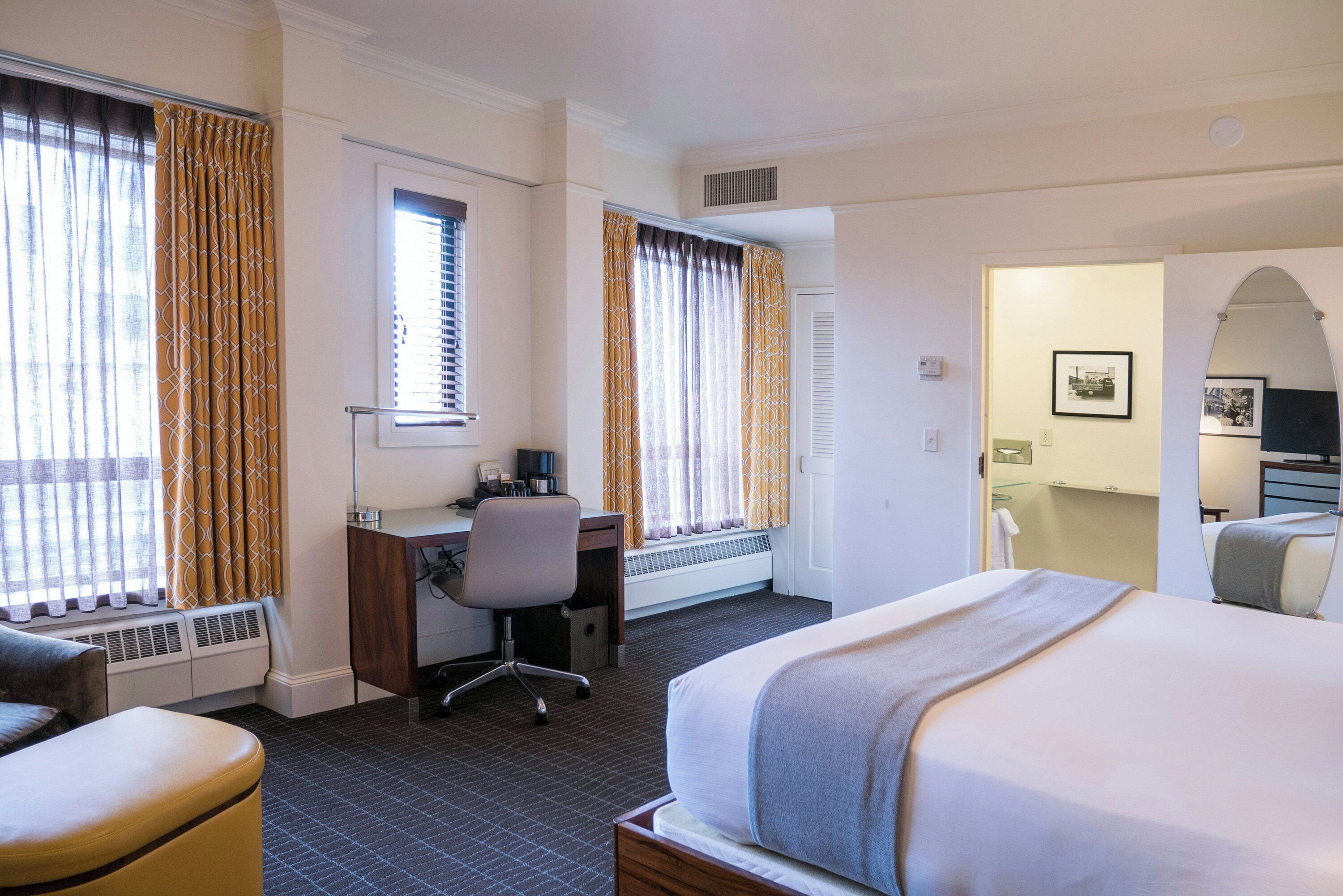 Habitación de hotel con cama, escritorio, silla y vistas al exterior a través de la ventana.