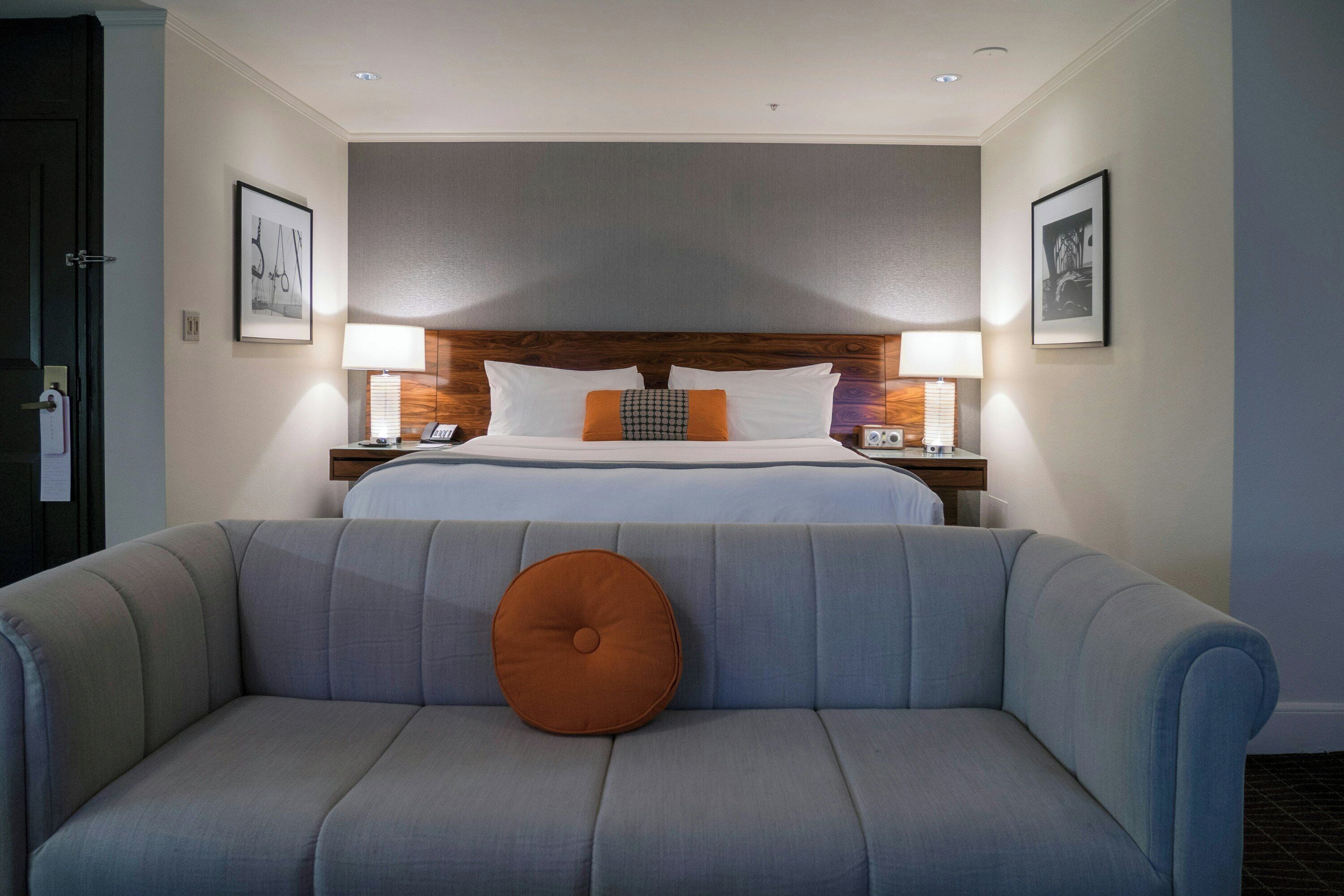 A hotel room with a bed, bedside tables, lamps, a sofa, and framed pictures on the walls.