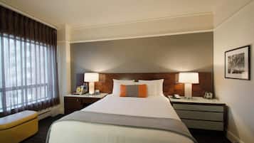 Habitación de hotel con una cama grande, dos mesitas de noche, una silla y un ventanal con cortinas.