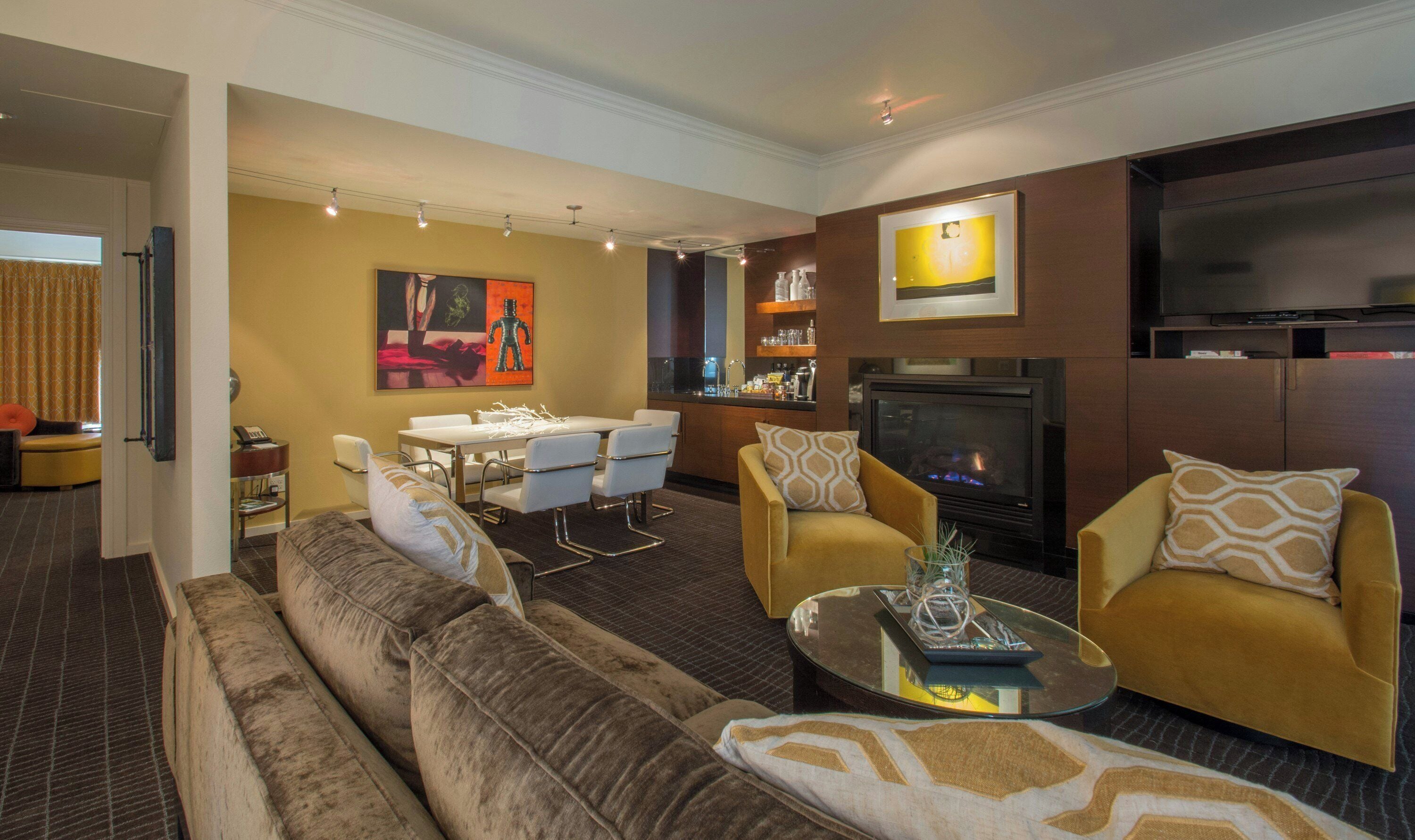A living room with a sofa, armchairs, a coffee table, a dining area with chairs, a fireplace, and a television.