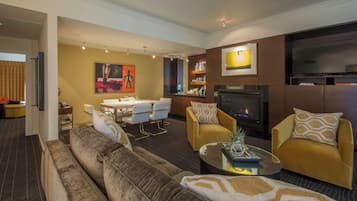 A living room with a sofa, armchairs, a coffee table, a dining area with chairs, a fireplace, and a television.