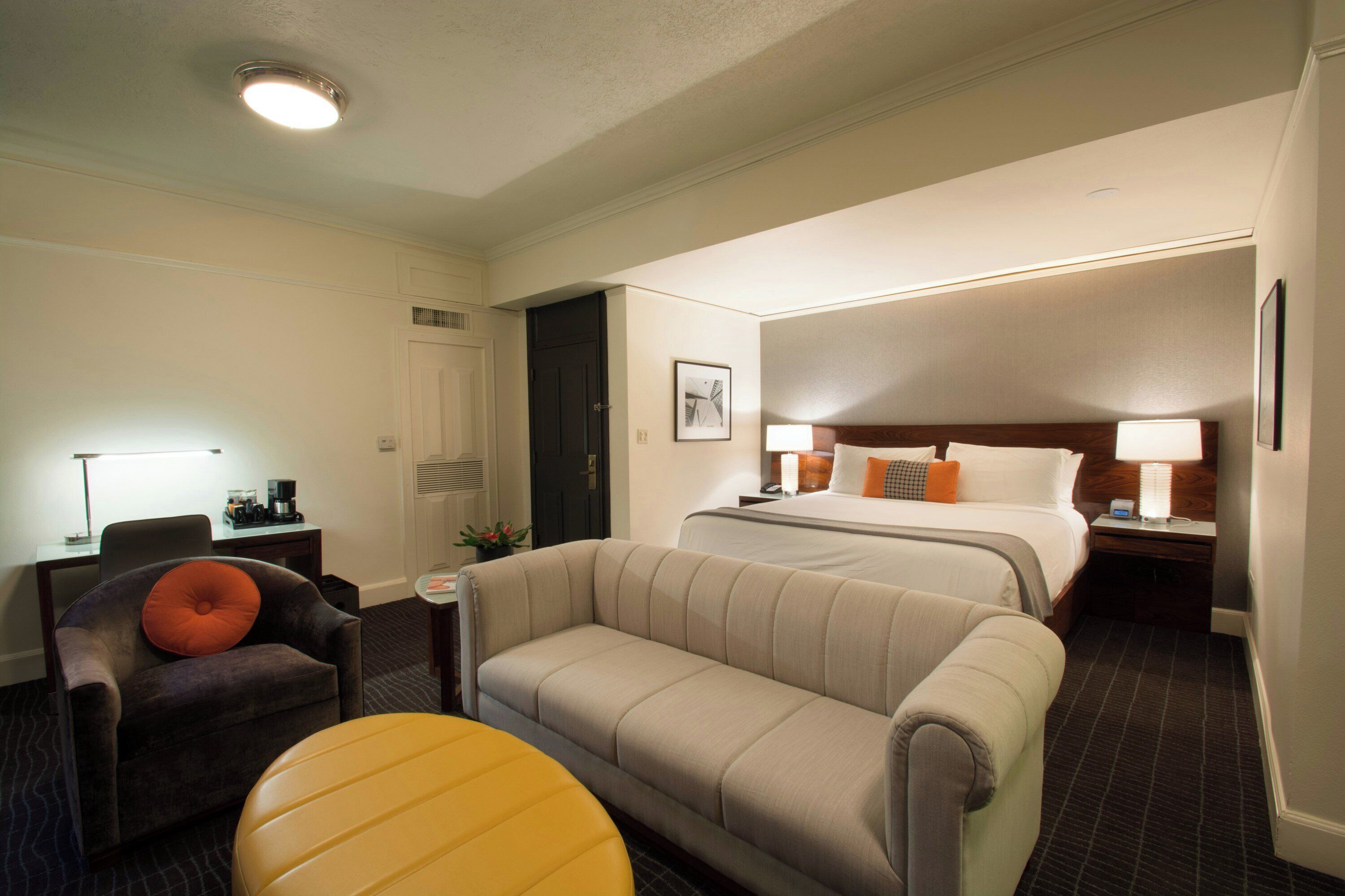 Una habitación de hotel con cama, sofá, sillón, mesita y lámpara.