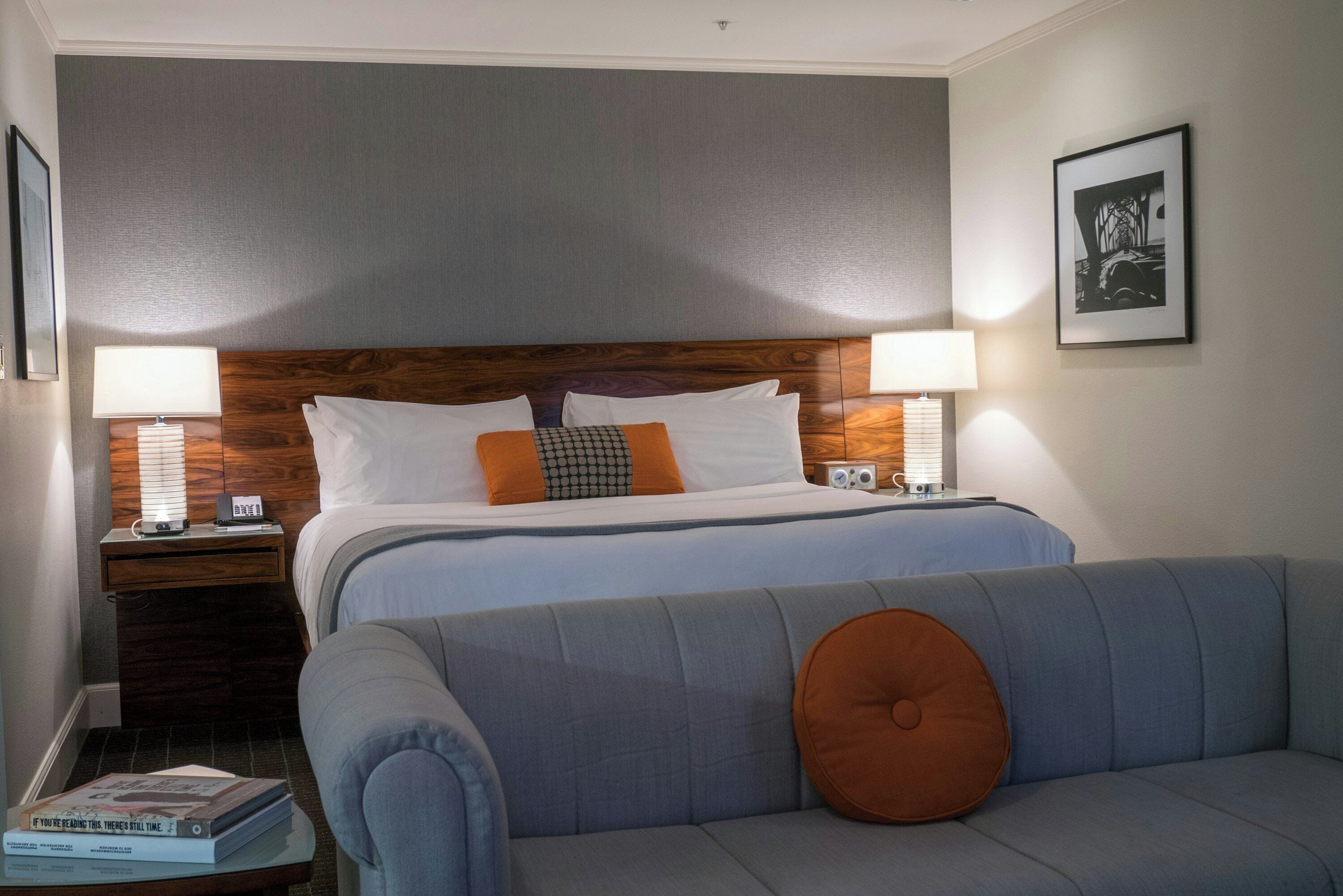 A hotel room with a bed, two bedside tables, a nightstand, a sofa, and a framed picture on the wall.