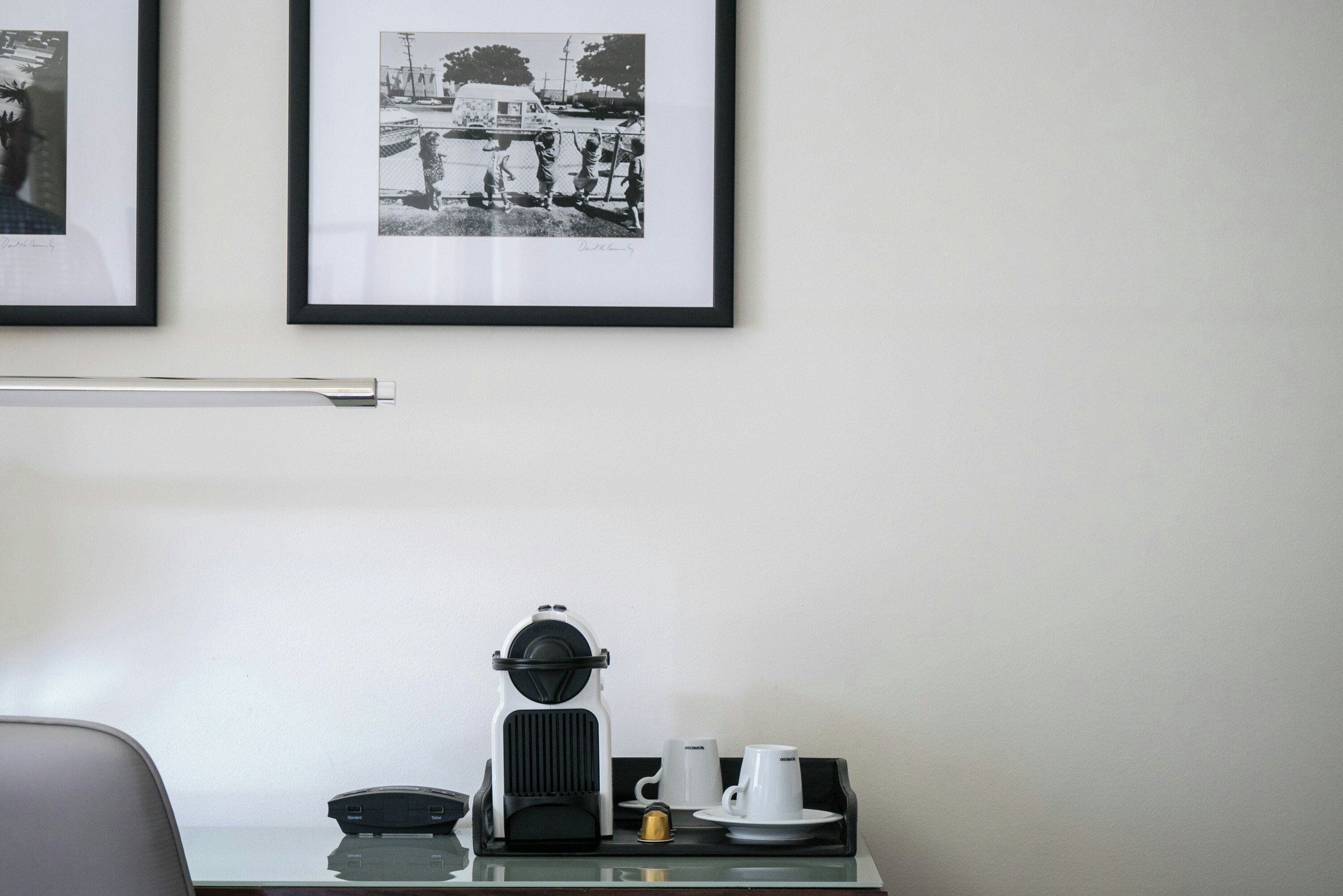Une chambre d’hôtel avec une photo en noir et blanc encadrée accrochée au mur, une machine à café et un plateau avec des tasses et un petit récipient.