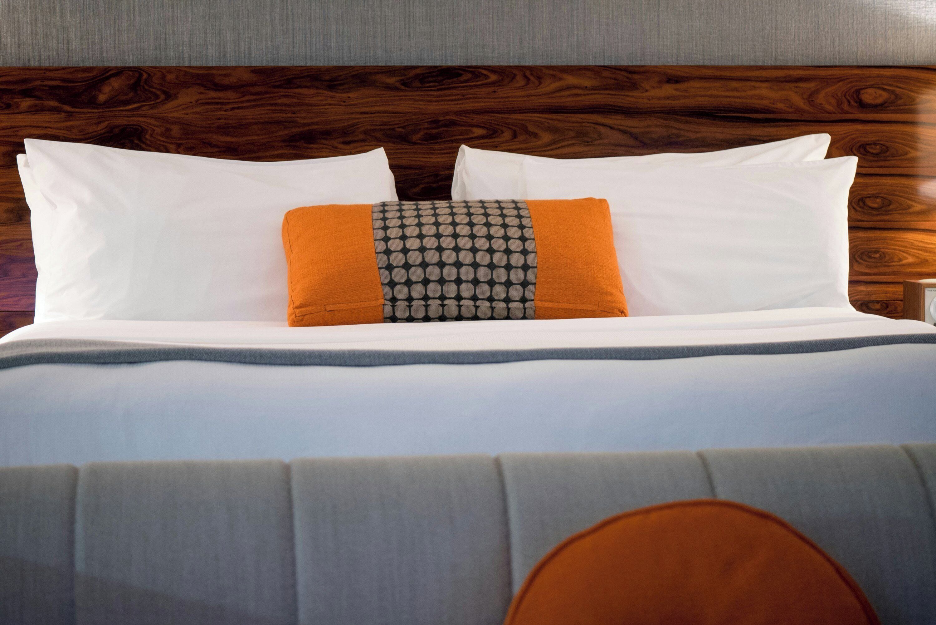 A neatly made bed with white bedding and two pillows, one with a geometric pattern.