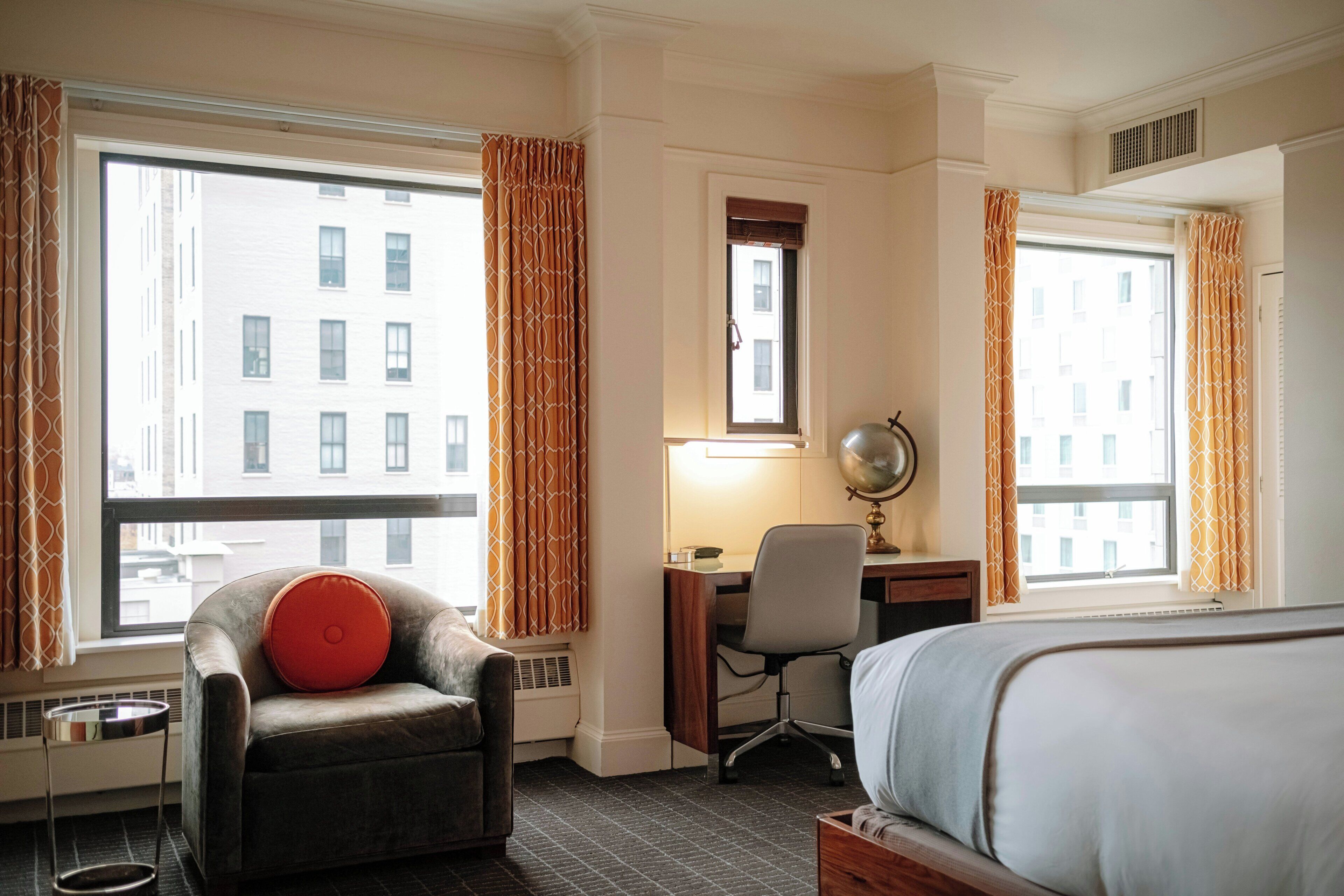 A hotel room with a bed, a desk, a chair, and a view of the city.