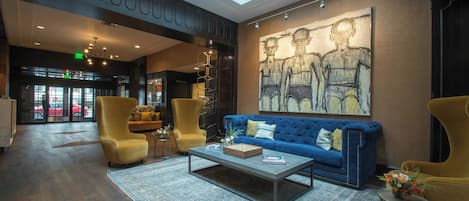 A modern lobby with a blue sofa, yellow armchairs, a coffee table, and a large abstract painting on the wall.