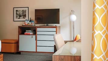 A hotel room with a television, a desk, a chair, a small cabinet, and a patterned carpet.