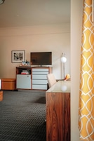 Une chambre d’hôtel équipée d’une télévision, d’un bureau, d’une chaise, d’une petite armoire et d’un tapis à motifs.