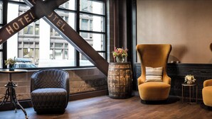 Eine Hotelhalle mit zwei Sesseln, einem kleinen Tisch, einer dekorativen Weinfass und einem großen Fenster mit Blick auf Gebäude.