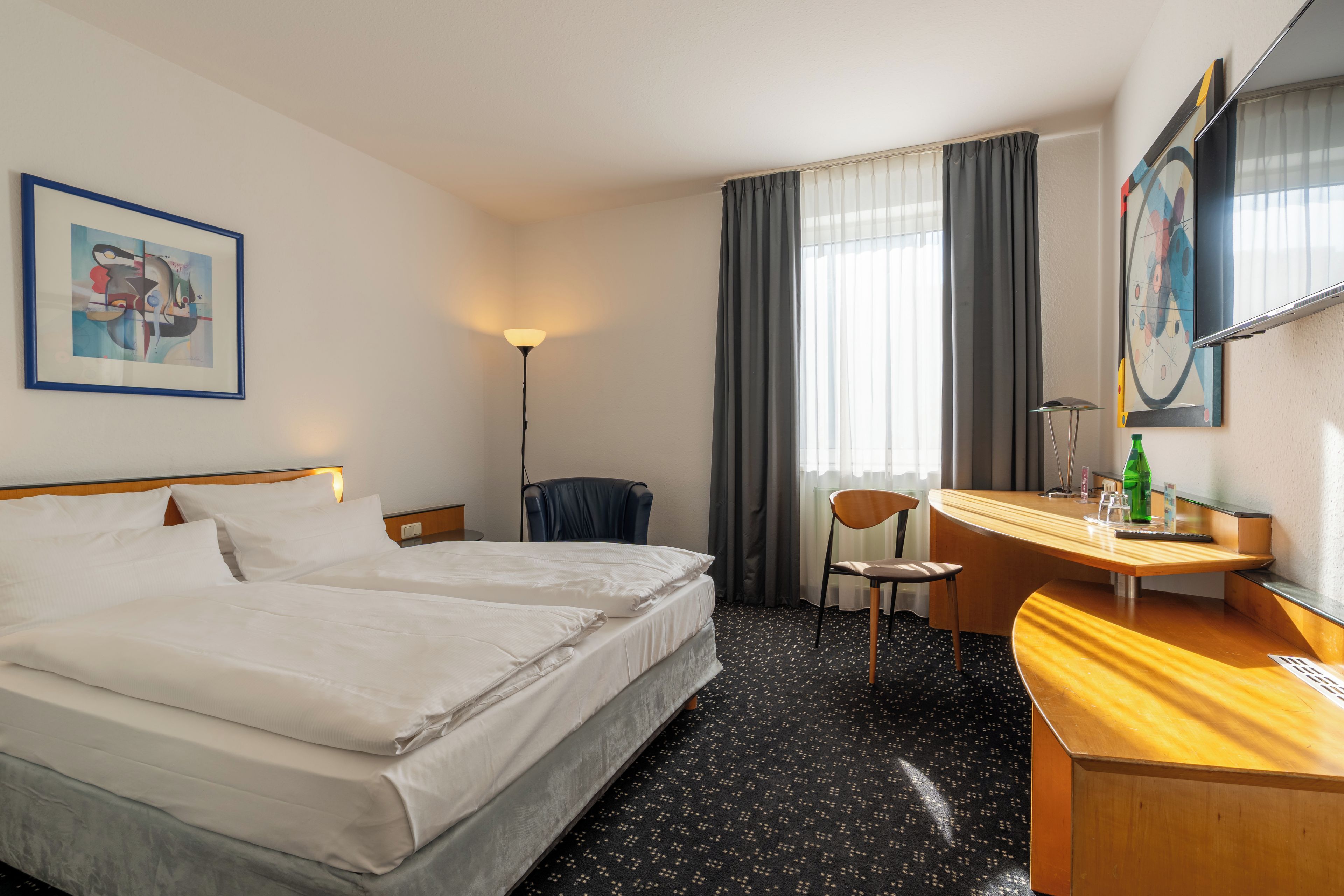 Una habitación de hotel con una cama, un escritorio, una silla, una lámpara y un cuadro en la pared.