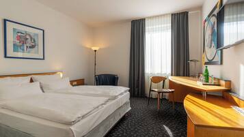 Una habitación de hotel con una cama, un escritorio, una silla, una lámpara y un cuadro en la pared.