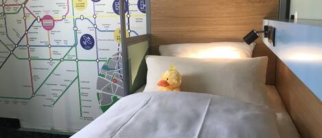 A hotel room with a bed, pillows, a plush toy, and a map of the city on the wall.