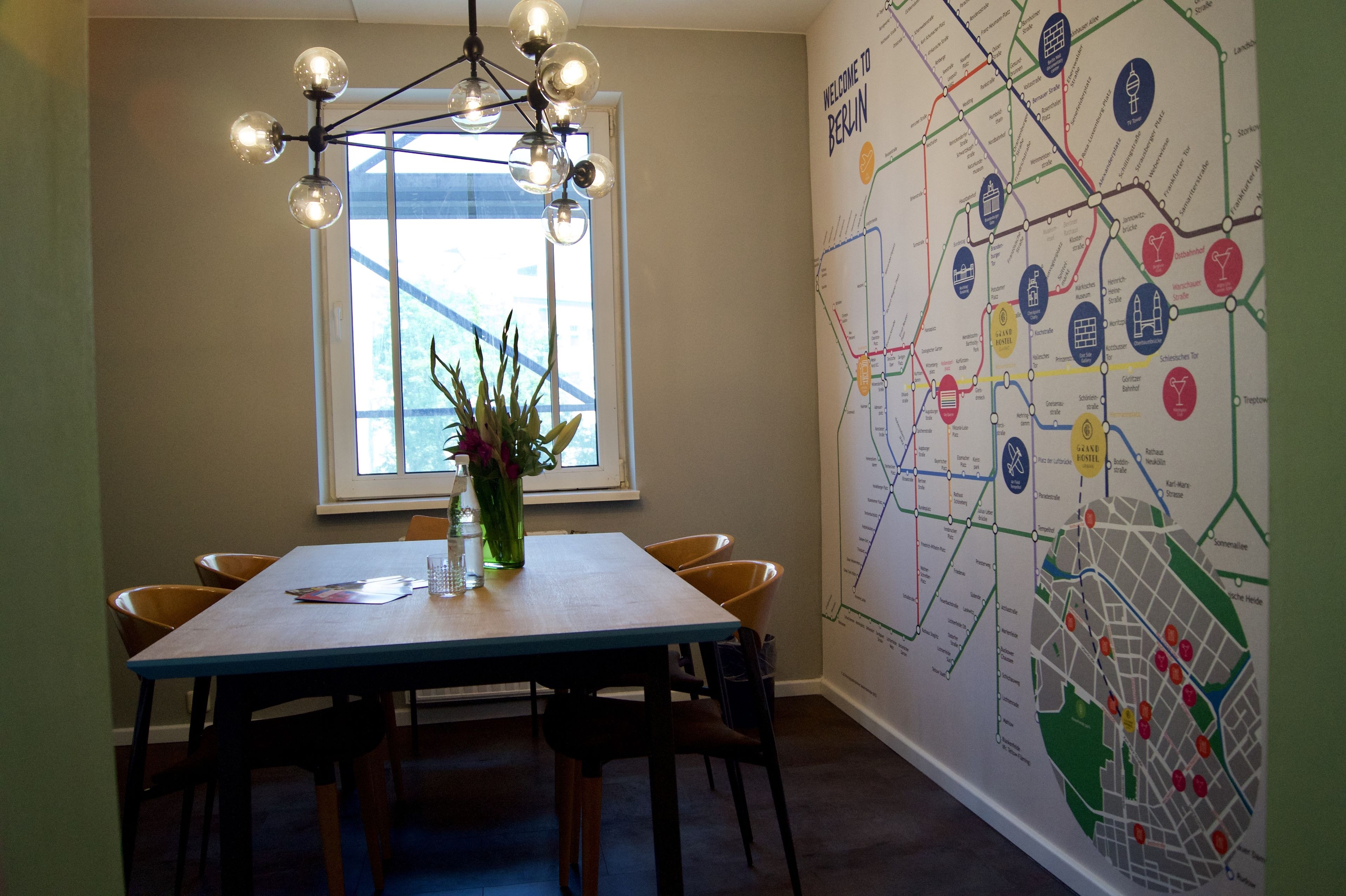 Un comedor con una mesa de madera, sillas, un jarrón con flores, una lámpara colgante y un mapa en la pared.