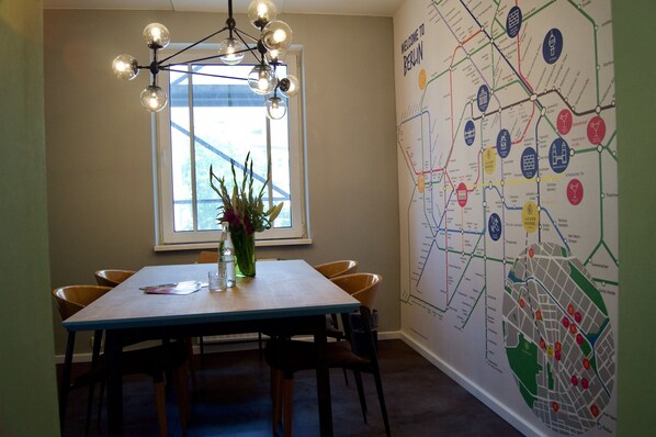 Un comedor con una mesa de madera, sillas, un jarrón con flores, una lámpara colgante y un mapa en la pared.