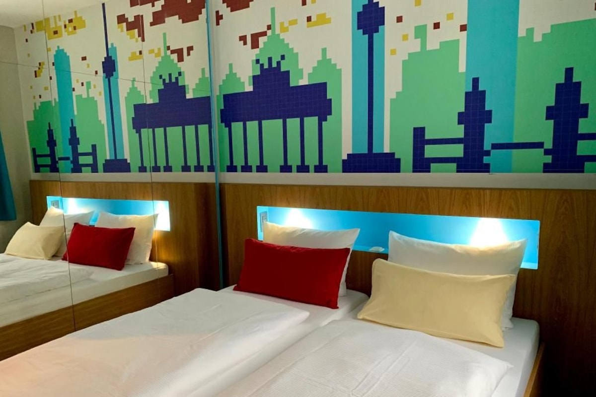 Habitación de hotel con dos camas, cada una con cabecera de madera, ropa de cama blanca y almohadas rojas y blancas.