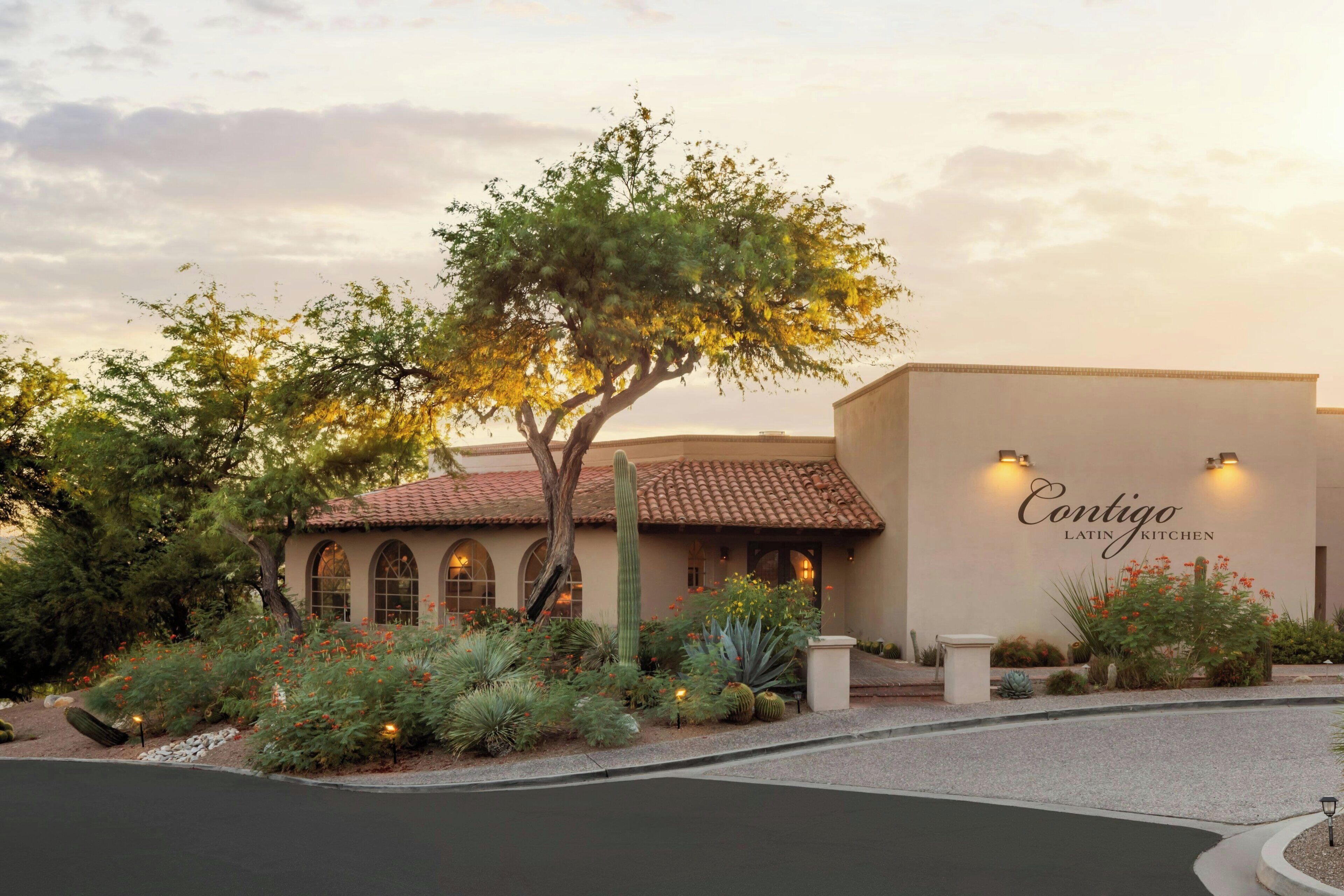A building with a sign reading "Contigo Latin Kitchen" surrounded by landscaped gardens and a curved driveway.