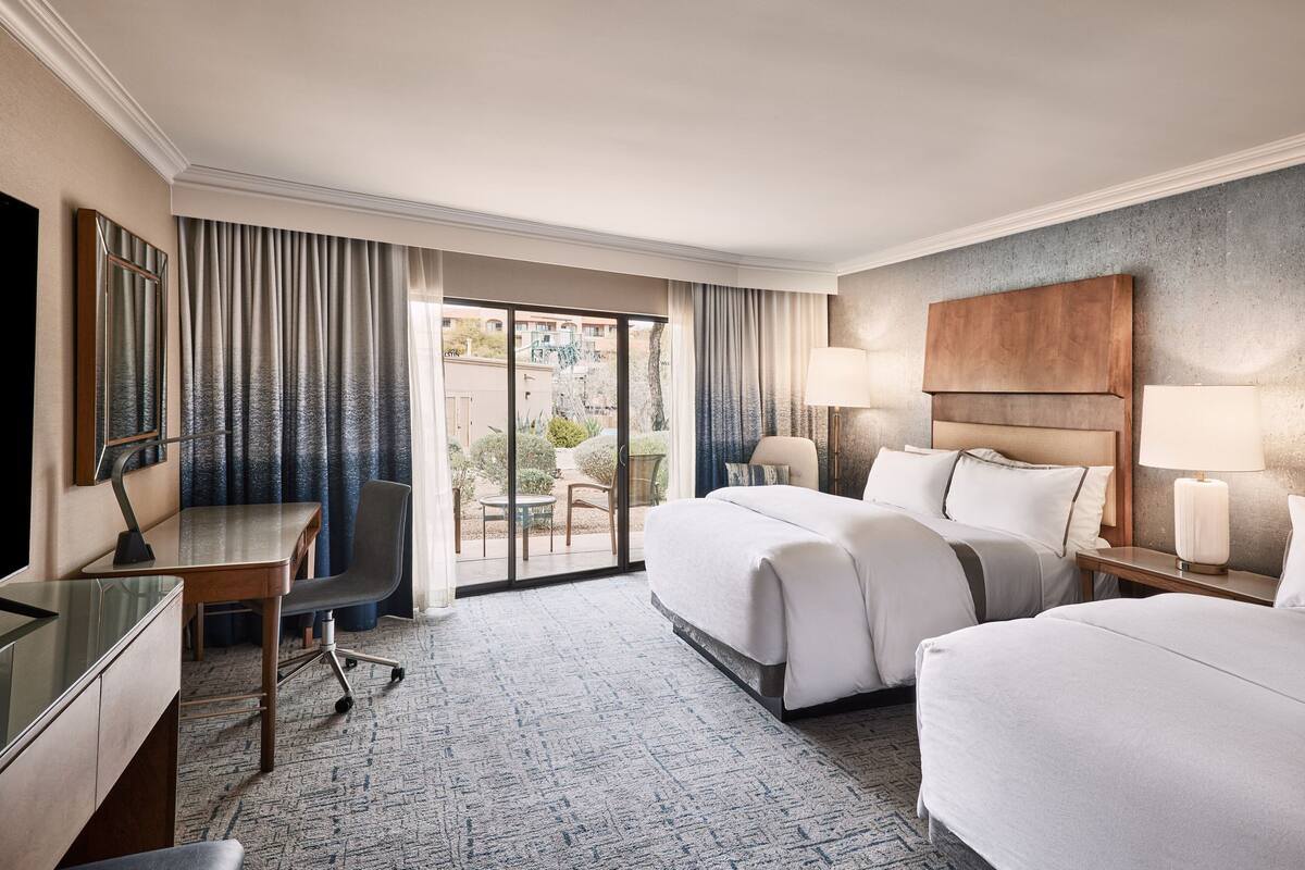 Une chambre d’hôtel équipée d’un bureau, de deux lits, d’une télévision et offrant une vue sur l’extérieur.