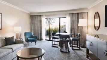 A hotel room with a sofa, two armchairs, a round table, a cabinet, and a large window with curtains.
