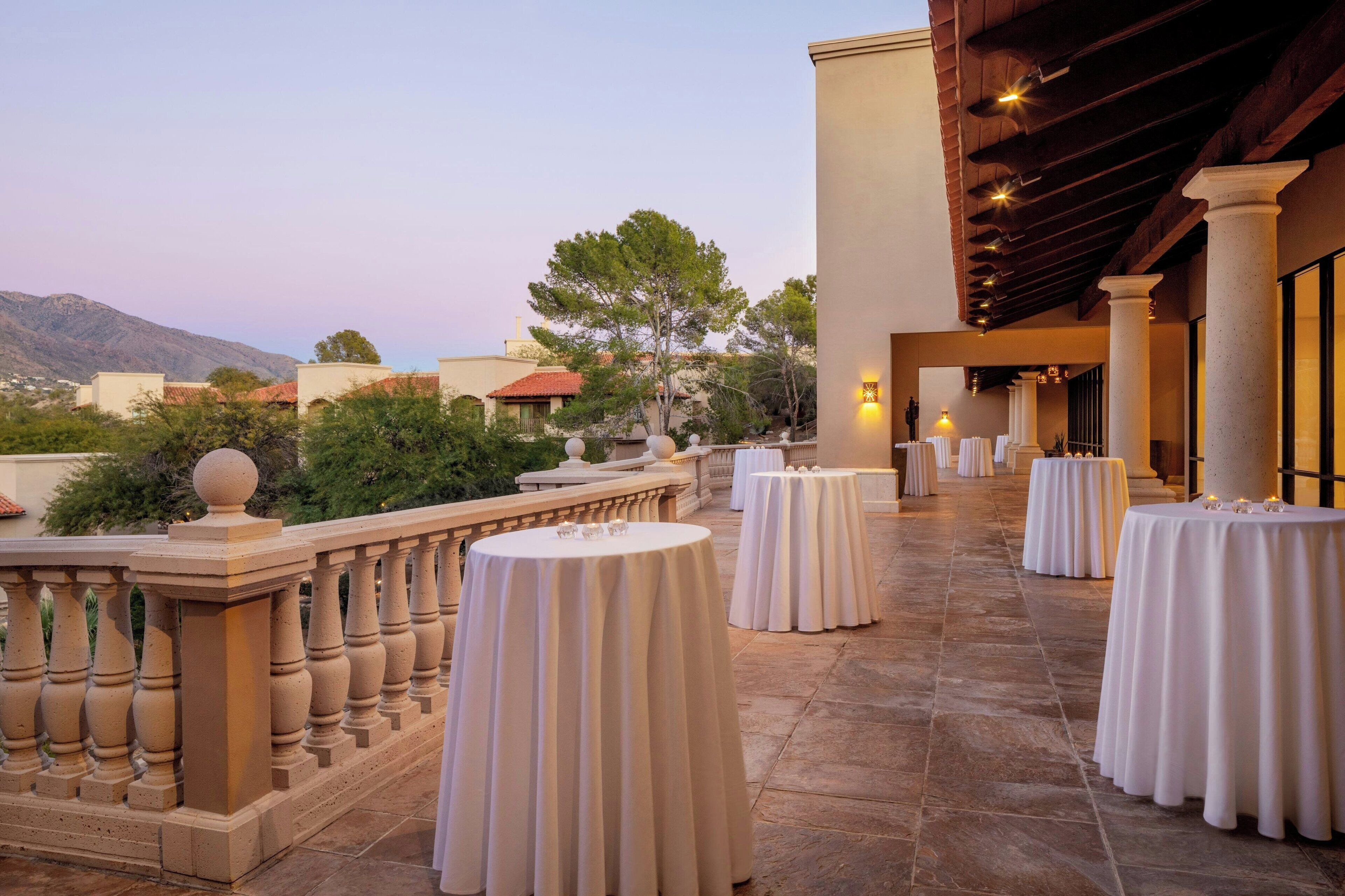 A terrace with round tables, a balustrade, and a view of mountains.