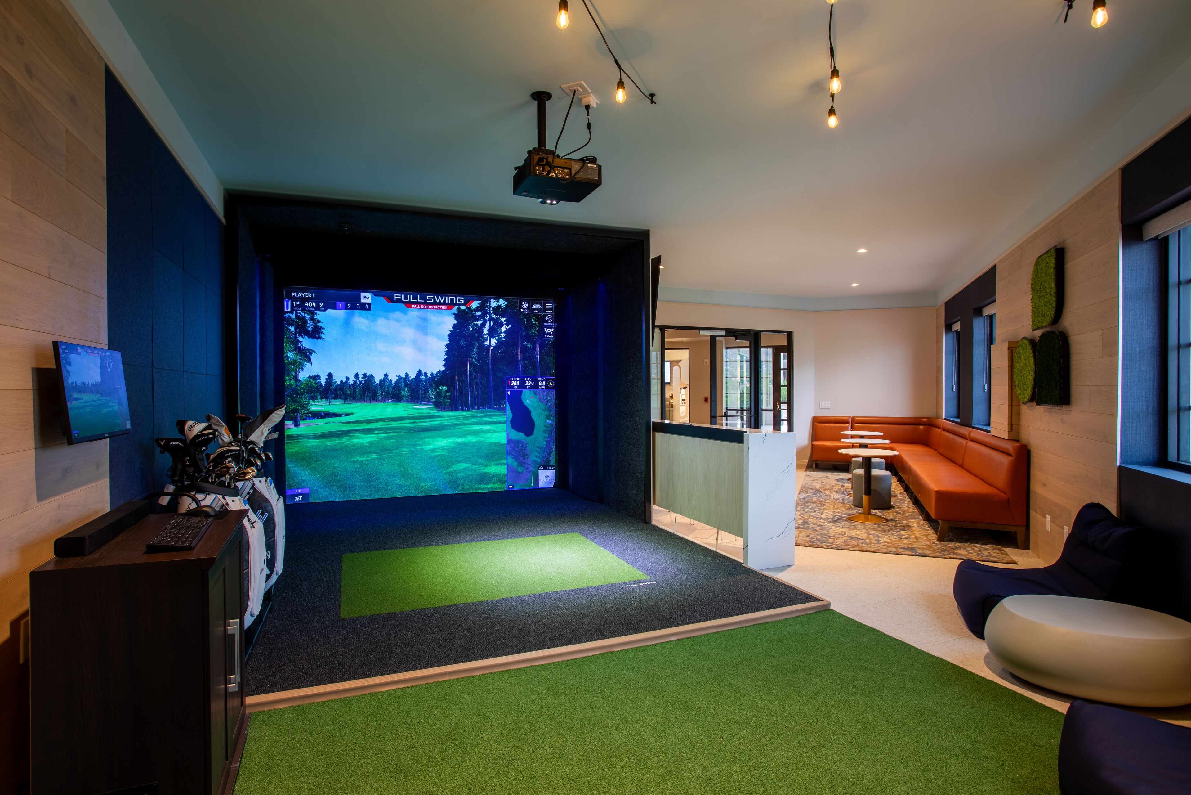 A modern room with a large screen displaying a golf game, a desk with a keyboard, and a seating area with a sofa and chairs.