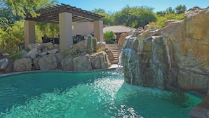 Un espace piscine agrémenté d’une pergola, de formations rocheuses et d’une cascade.