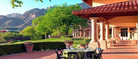 Un espace extérieur aménagé pour les repas, avec des tables dressées, entouré d’un jardin agrémenté de plantes en pot et offrant une vue sur les montagnes.