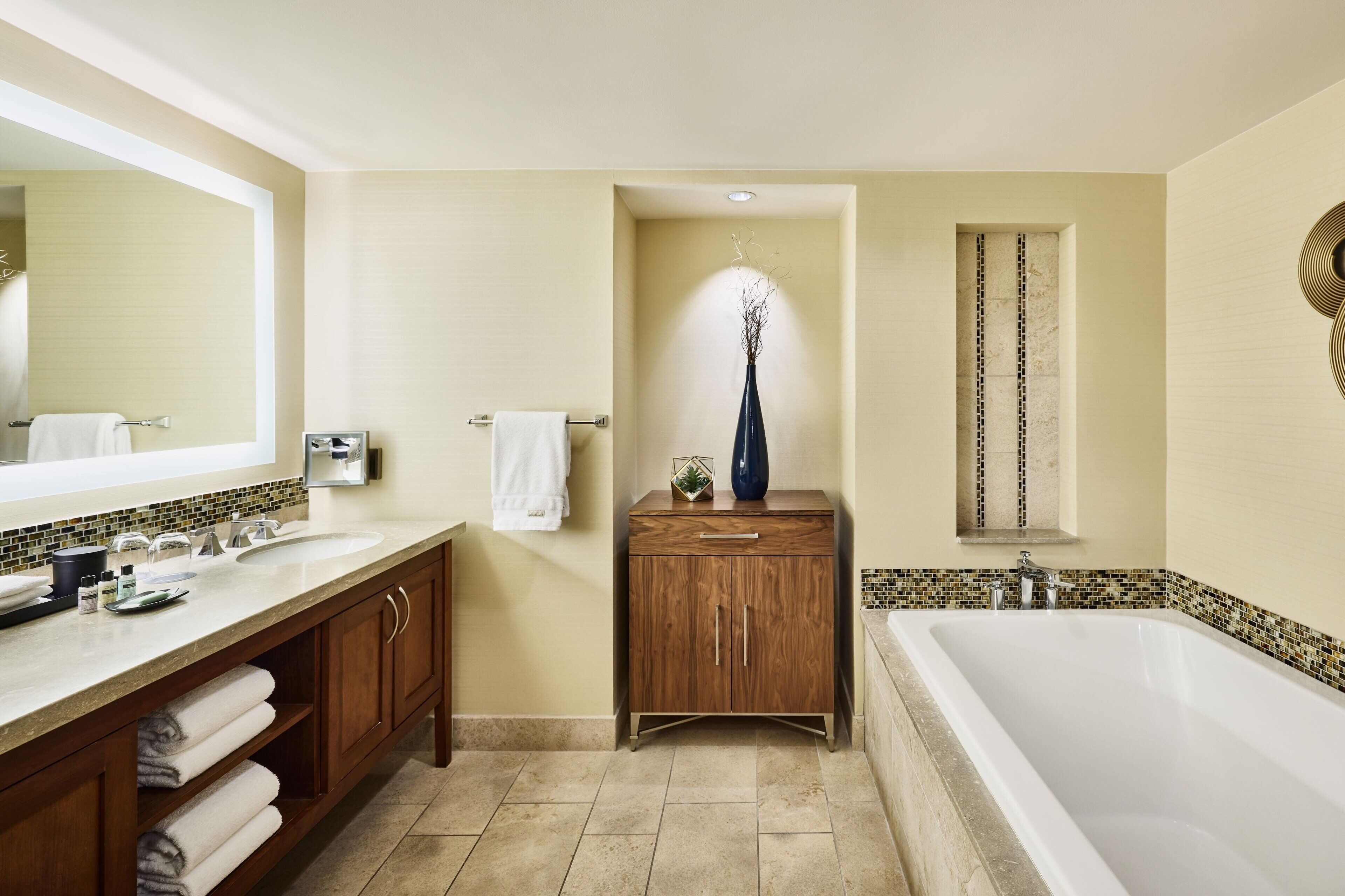 Un bagno moderno con un ampio specchio, due lavabi, un mobile contenitore in legno e una vasca da bagno freestanding.