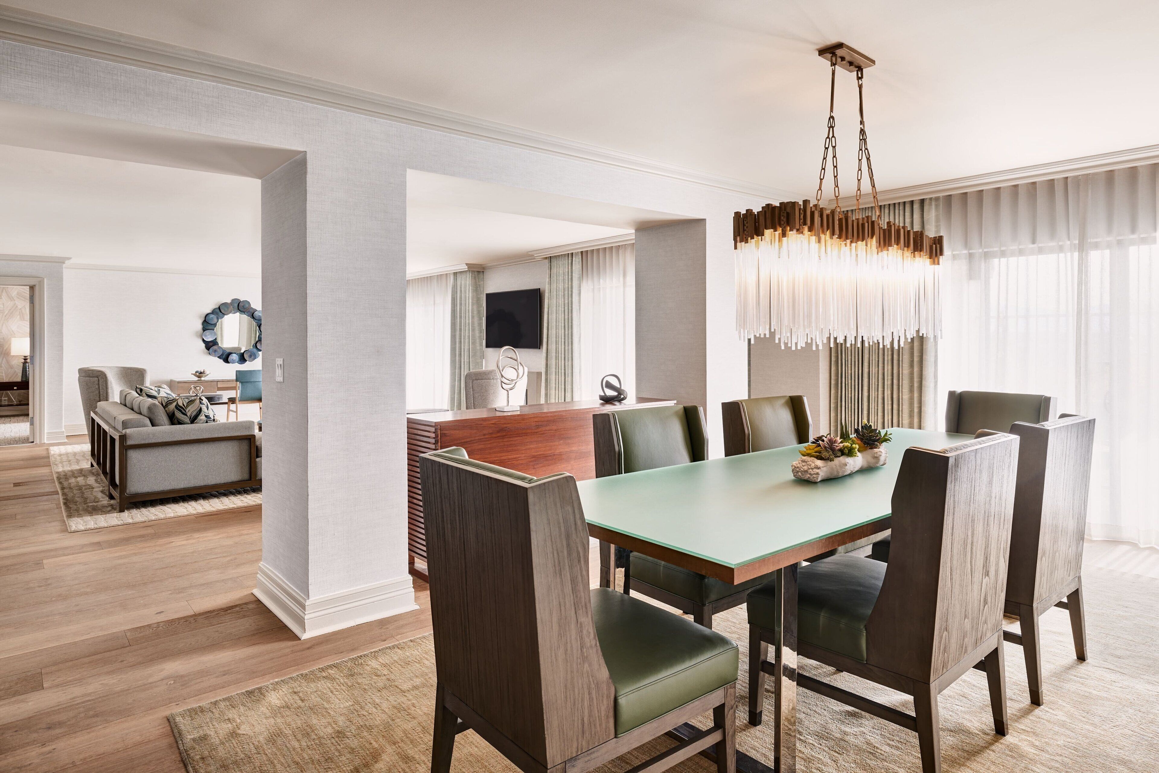 A modern dining area with a glass table, dark wooden chairs, and a hanging light fixture.
