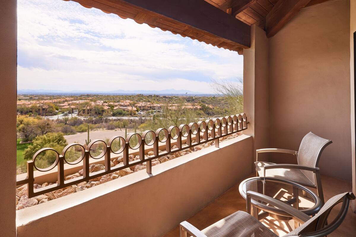 Un balcon donnant sur la ville, avec une balustrade en métal et deux chaises.