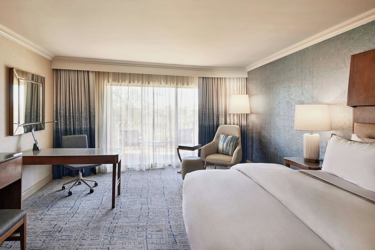 Une chambre d’hôtel avec un grand lit, un bureau, une chaise, une lampe et une vue sur l’extérieur par la fenêtre.